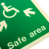 Close up of a safe area sign rigid plastic showing a green background with white accessible wheelchair symbol and arrows pointing in three directions