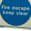 Closeup of a fire escape keep clear sign showing white text on a blue circle background