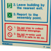 Closeup of a fire action sign showing safety instructions in blue and red text with symbols
