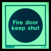 Fire door keep shut sign made of rigid plastic glowing in the dark with white text on a black circle background