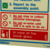 Closeup of a fire action sign showing safety instructions and a break glass notice in red and white