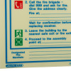 Closeup of fire action sign showing emergency instructions with call fire brigade and evacuation details in blue text