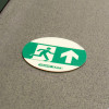 fire exit floor disc self adhesive showing a green running man symbol and an arrow on a grey floor