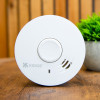 White Ke10Y29 Kidde 10Y29 10 Year Optical Smoke Alarm on a wooden surface with a plant in the background