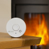 Kidde 10Y29 10 Year Optical Smoke Alarm on a wooden table with a fireplace burning in the background