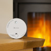 Kidde 2030-DSR Battery Optical Smoke Alarm on a wooden table with a fireplace burning in the background