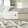Kidde K10LLCO 10 Year Carbon Monoxide Alarm on a table with a beige sofa and blanket in the background