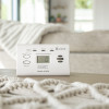Kidde K7DCO Digital Travel Carbon Monoxide Alarm on a table with a beige sofa and blanket in the background