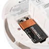 A close-up of a smoke alarm’s open battery compartment with a fitted 9V Duracell battery and printed safety instructions inside the casing.