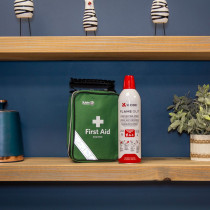 Green St John Ambulance first aid kit and Kidde Flame Out fire‑fighting spray displayed on a wooden shelf with decorative items