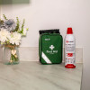 Green St John Ambulance first aid kit and Kidde Flame Out fire‑fighting spray on a countertop next to a textured glass vase with artificial flowers