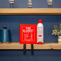 Red UltraFire fire blanket and Kidde Flame Out fire‑fighting spray on a wooden shelf with a teal container and a small potted plant.