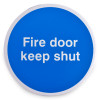 Front view of a round blue fire door keep shut metal sign with white text and self adhesive backing