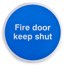 Front view of a round blue fire door keep shut metal sign with white text and self adhesive backing