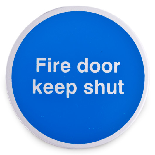Front view of a round blue fire door keep shut metal sign with white text and self adhesive backing