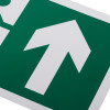 close up of white rigid plastic self adhesive fire exit sign showing a white arrow pointing upwards on a green background