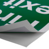 Partially peeled fire exit sign eec directive self adhesive down showing backing paper and green surface