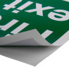 Close-up of fire exit sign eec directive self adhesive up left partially peeled from surface showing backing paper