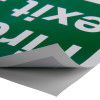 Close up of a fire exit sign eec directive self adhesive up with the corner peeled back showing the adhesive side