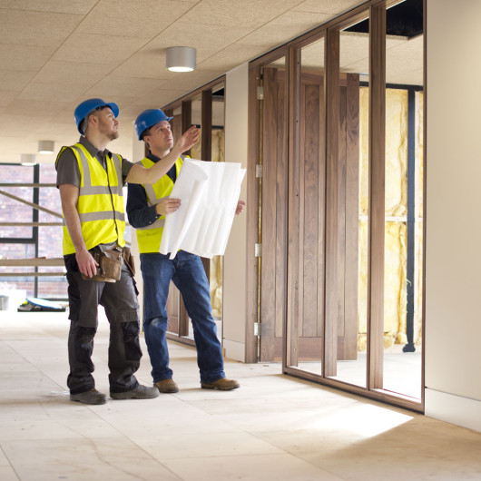 surveyors in a building under construction with plans looking at a wall