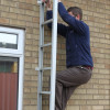 Man climbing down Saffold Fold Out Fire Escape Ladder against brick wall near window