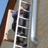 Man climbing Saffold Fold Out Fire Escape Ladder through an open window against a brick wall