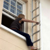 Woman climbing out of a window onto the Saffold Fold Out Fire Escape Ladder Window Escape attached to a building wall