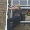 Woman climbing down the Saffold Fold Out Fire Escape Ladder from a window on a brick building with flowers on the sill
