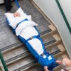 Person strapped into a spectrum healthcare ski sled being carried down stairs by two people