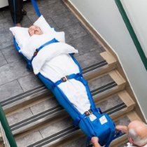 Person strapped into a spectrum healthcare ski sled being carried down stairs by two people