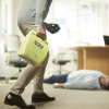 Person carrying a green Zoll Aed Plus Defibrillator with a person lying on the floor in background