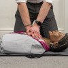 Hands performing compressions on laerdal little anne qcpr dark training manikin lying on the floor