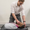 Man kneeling and adjusting laerdal little anne qcpr dark training manikin lying on the floor during training session