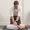 Person performing compressions on laerdal little anne qcpr light training manikin lying on the floor