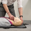 Person demonstrating head tilt on laerdal little anne qcpr light training manikin lying on a grey mat