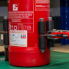 Close up of an Ultrafire extinguisher servicing clamp attached to a red fire extinguisher body on a green surface