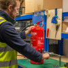 Engineer working close up with an ultrafire extinguisher servicing clamp and a red fire extinguisher on a workbench