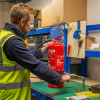 Engineer using ultrafire extinguisher servicing clamp on a fire extinguisher in a workshop setting