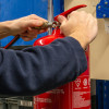 Hands using ultrafire extinguisher servicing clamp for hose inspection on a red fire extinguisher