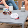 carbon monoxide detector on a grey table with sunglasses and mugs, family sitting in the background