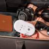 White carbon monoxide detector placed inside an open suitcase with camera, sunglasses, headphones and passport nearby