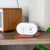sealed 10 year carbon monoxide detector with a red and white strap placed on a wooden shelf next to a speaker