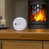 Close up of a white ultrafire ulls10 smoke alarm sitting on a wooden table with a glowing fireplace in the background