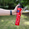 Hand holding a red Ultrafire Alpha aerosol extinguisher ready to use against a blurred green outdoor background