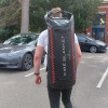 Person carrying a large black bag labelled fire blanket Bridgehill on their back in a car park