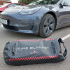 Car fire blanket for electric vehicles Bridgehill in its black and red bag on the ground near a dark grey electric car wheel