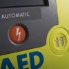 A close-up of the orange shock button on a bright green defibrillator